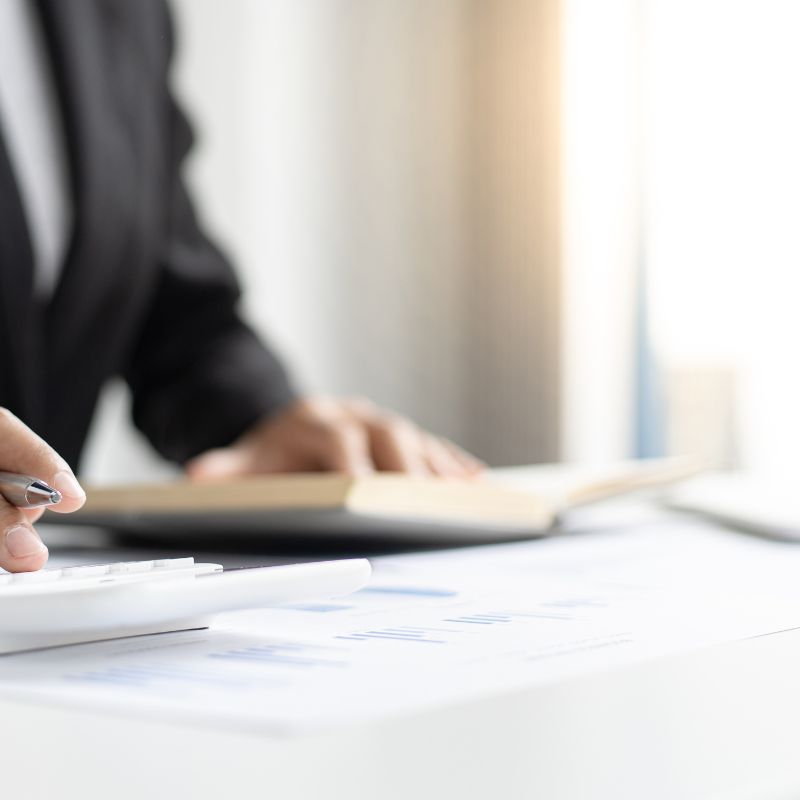 Une personne en costume tient un stylo et travaille sur des documents sur un bureau blanc. Un cahier est ouvert à côté d'elle. Une personne en costume tient un stylo et travaille sur des documents sur un bureau blanc. Un cahier est ouvert à côté d'elle.