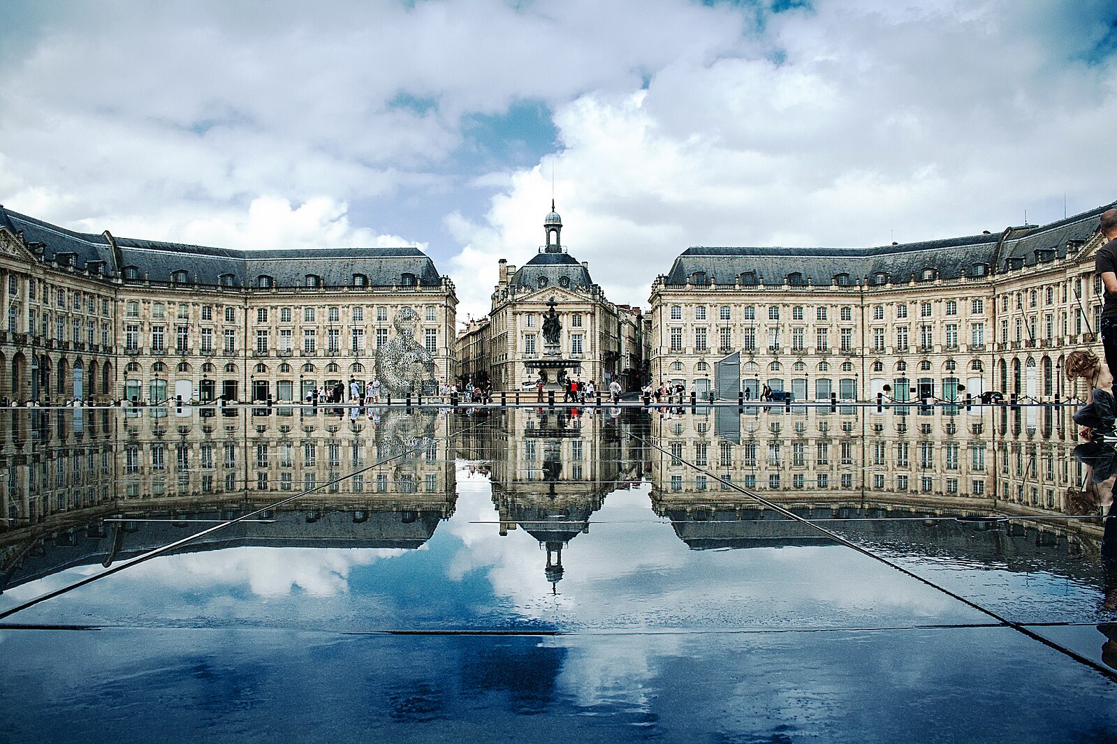 Bâtiments historiques se reflétant dans l'eau sur la Place de la Bourse à Bordeaux, en France, sous un ciel nuageux. Bâtiments historiques se reflétant dans l'eau sur la Place de la Bourse à Bordeaux, en France, sous un ciel nuageux.